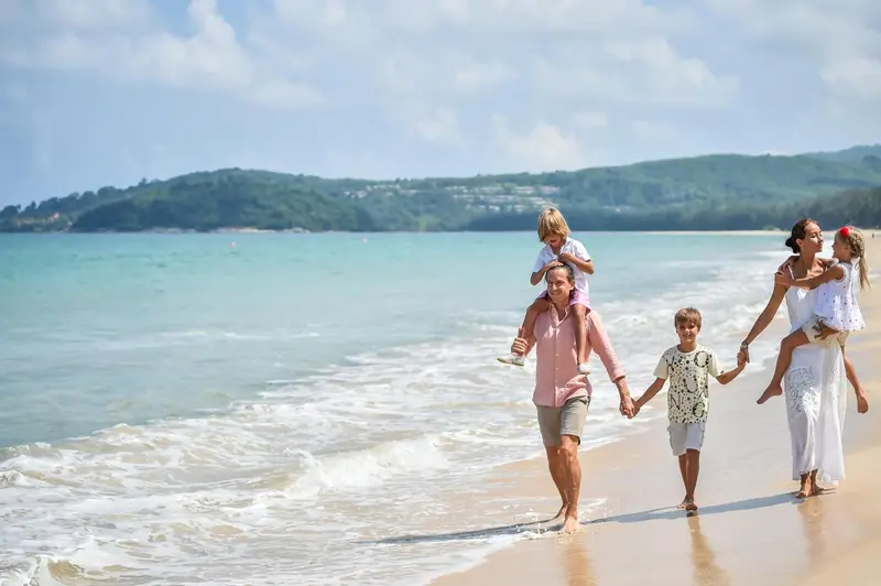 Une famille se promène sur une plage de sable fin, bordée par une mer turquoise.