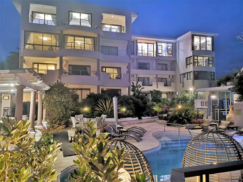 Bâtiment à plusieurs étages avec des balcons et une piscine éclairée la nuit.