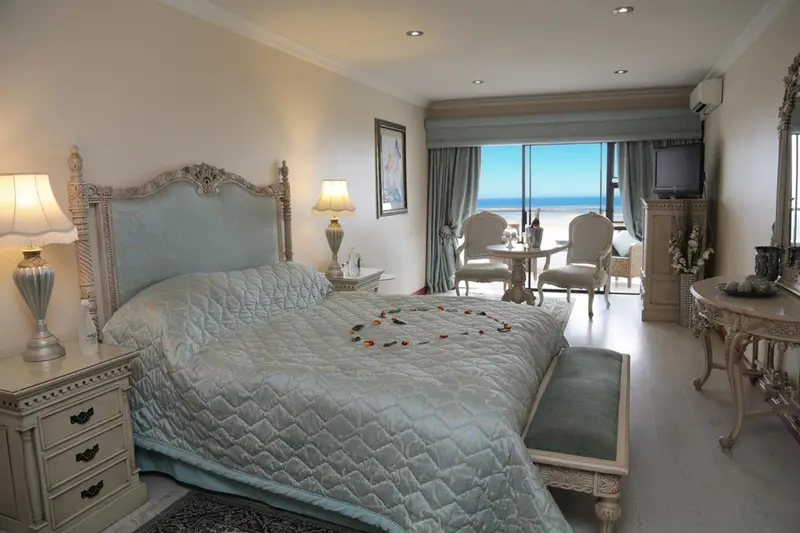 Chambre lumineuse avec un grand lit et un coin salon donnant sur la mer.