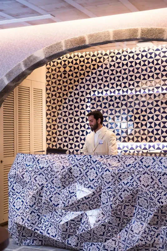 Un homme se tient derrière un comptoir décoré de motifs géométriques bleus et blancs.