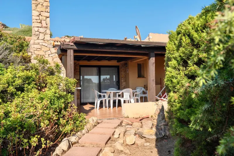 Terrasse ombragée avec table et chaises devant une habitation.