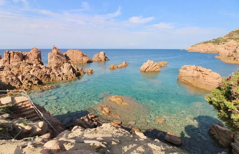 Une plage de sable et de roches rouges bordée d'une eau turquoise.