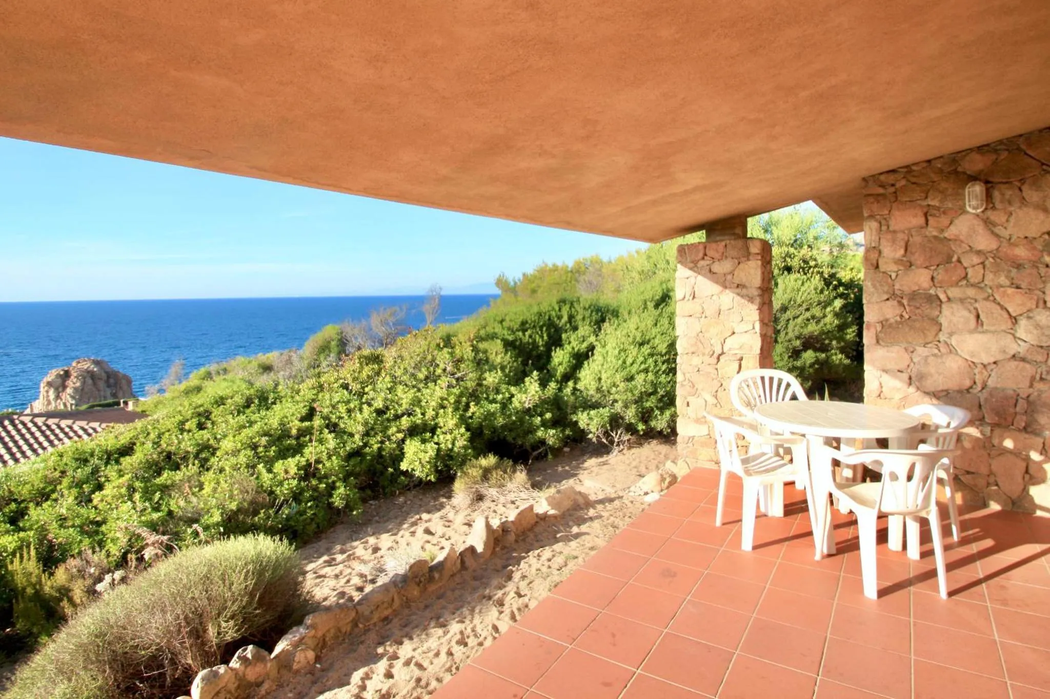 Terrasse ombragée avec table et chaises donnant sur la mer.