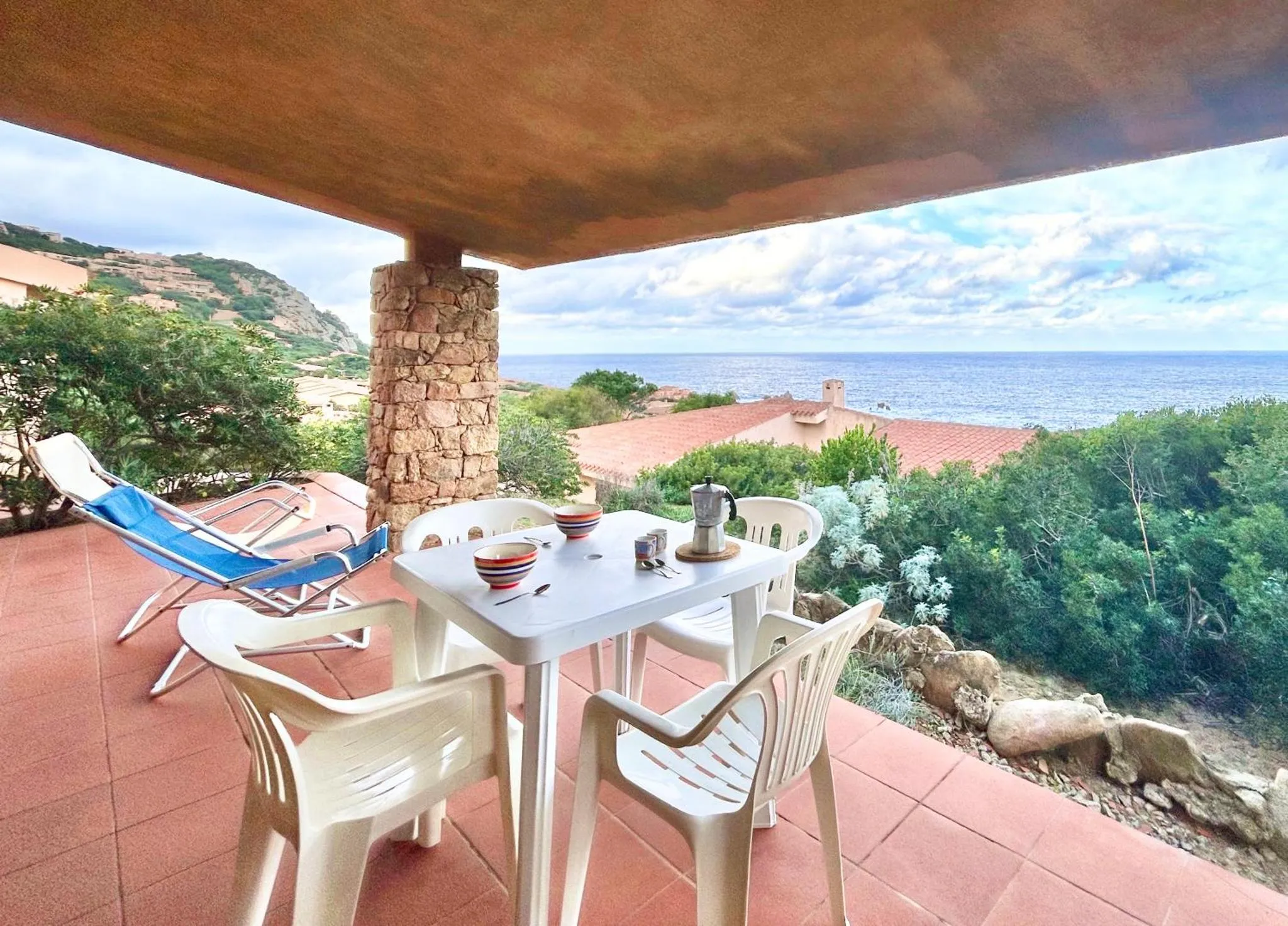 Terrasse avec table et chaises donnant sur la mer et les collines.