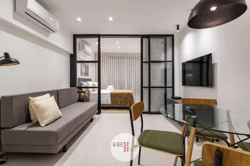 Un espace de vie moderne avec un canapé, une table et un lit visible à travers une cloison vitrée.