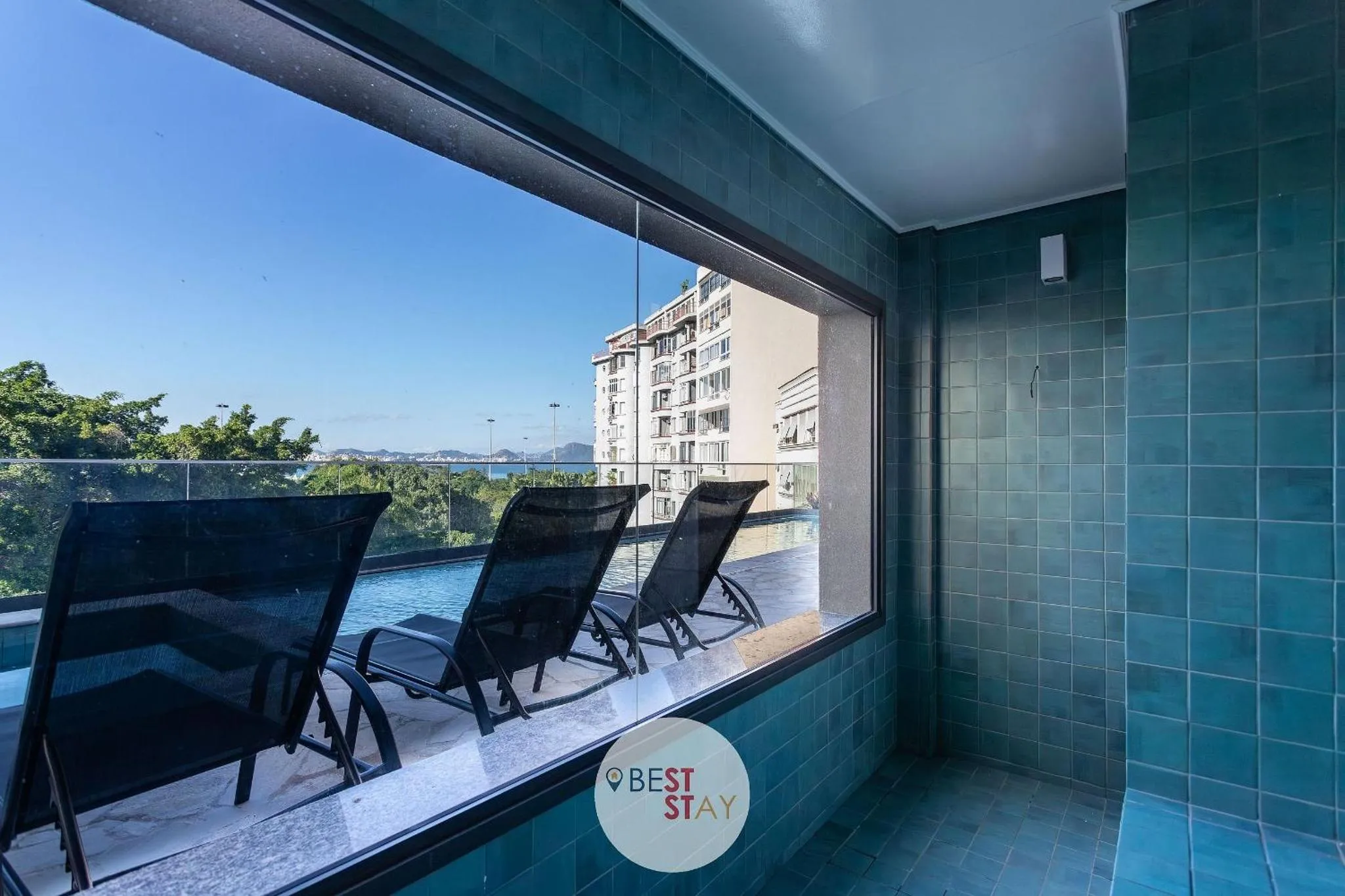 Transats noirs alignés au bord d'une piscine turquoise avec vue sur la mer.