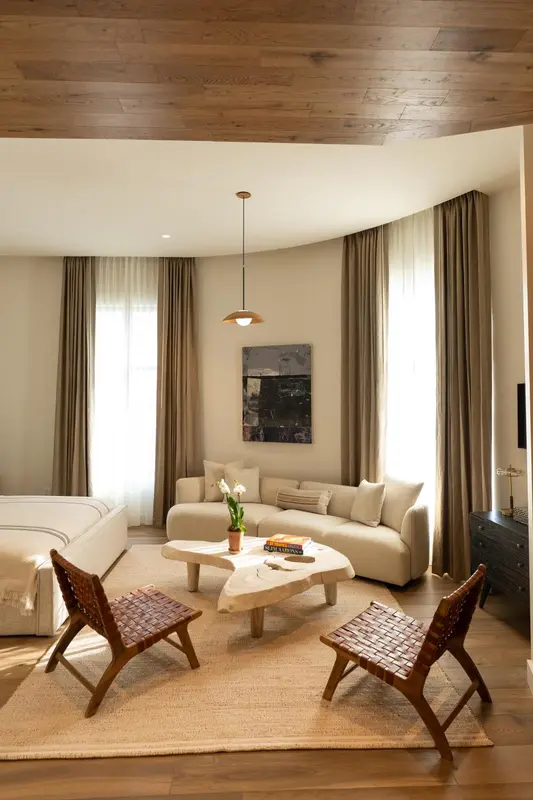Un salon clair avec un canapé incurvé, deux fauteuils en bois et une table basse.