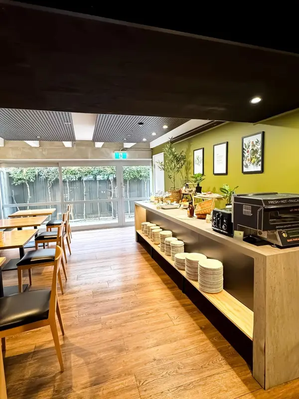 Une salle lumineuse avec des tables et des chaises, un buffet garni et une décoration végétale.