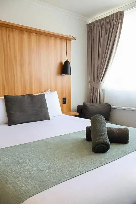 Lit préparé avec oreillers et couverture verte dans une chambre lumineuse.