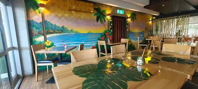 Une salle de restaurant lumineuse avec des tables dressées et une décoration tropicale sur les murs.