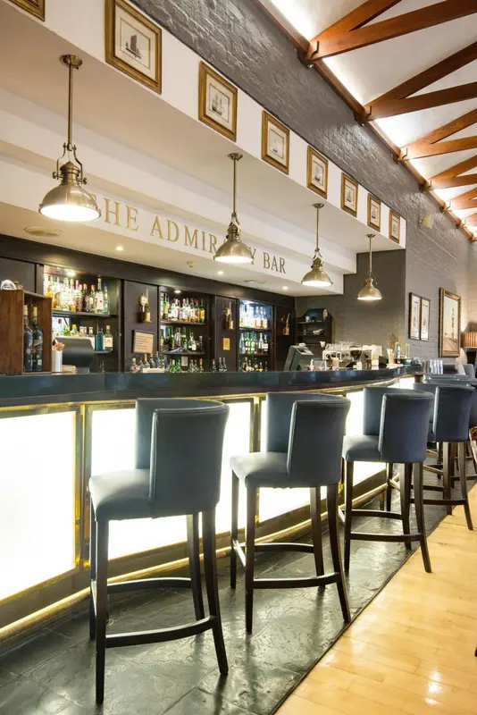 Un comptoir de bar moderne avec des tabourets et des bouteilles illuminées.