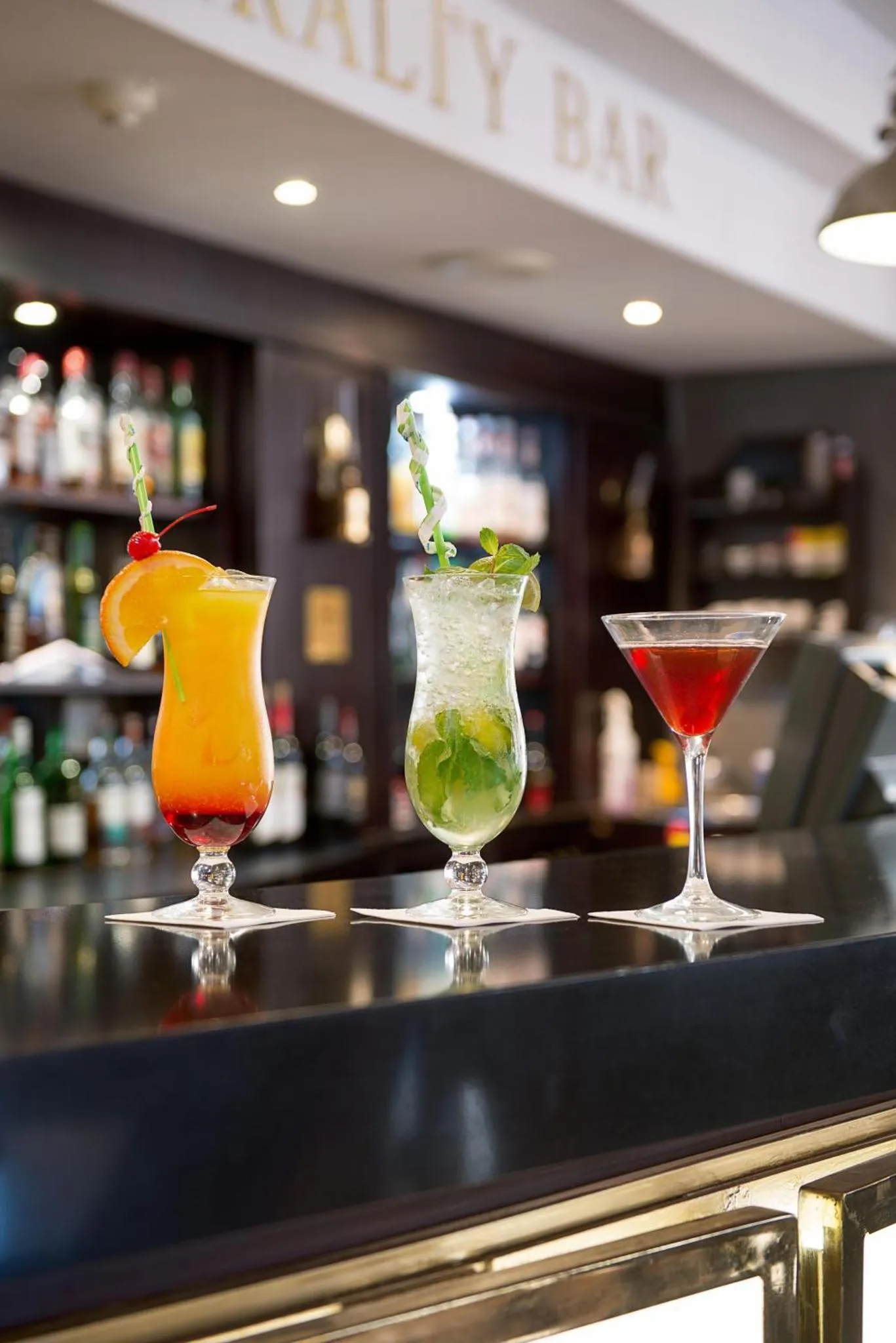Trois cocktails colorés sont présentés sur un comptoir de bar éclairé.