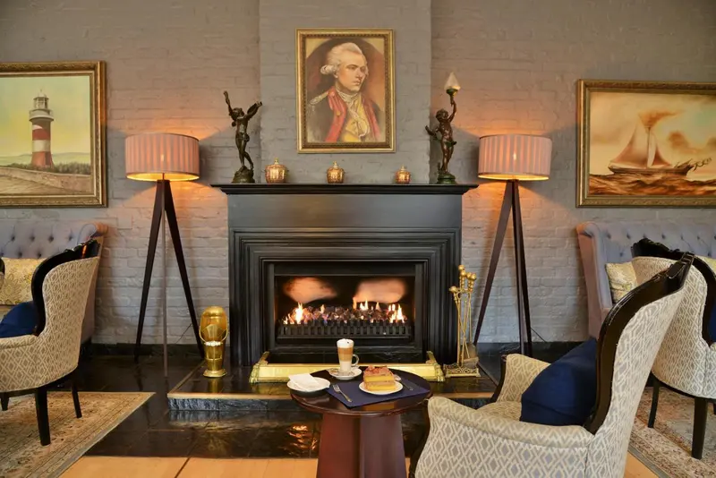Une cheminée décorative avec des tableaux et des lampes éclaire un coin salon avec des fauteuils et une table basse.