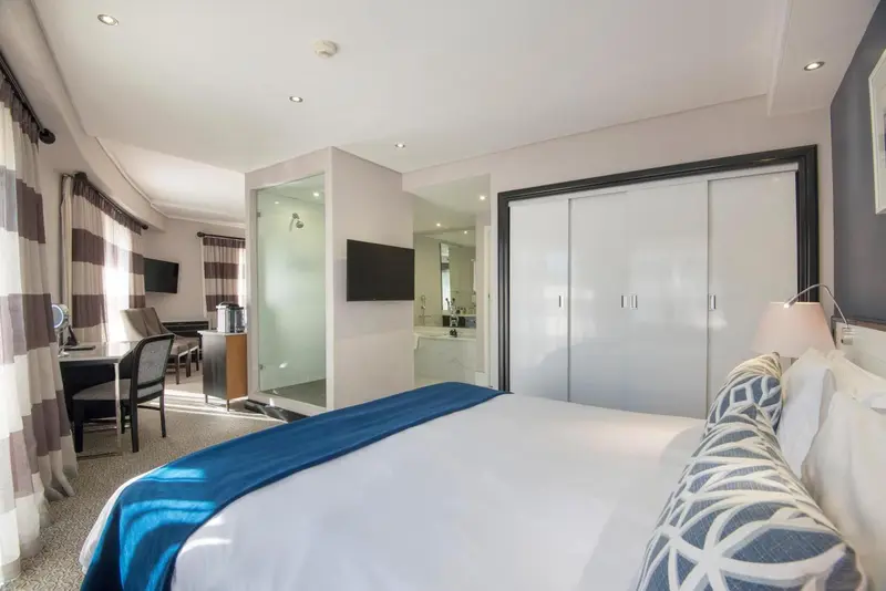 Chambre lumineuse avec un grand lit et un espace bureau.
