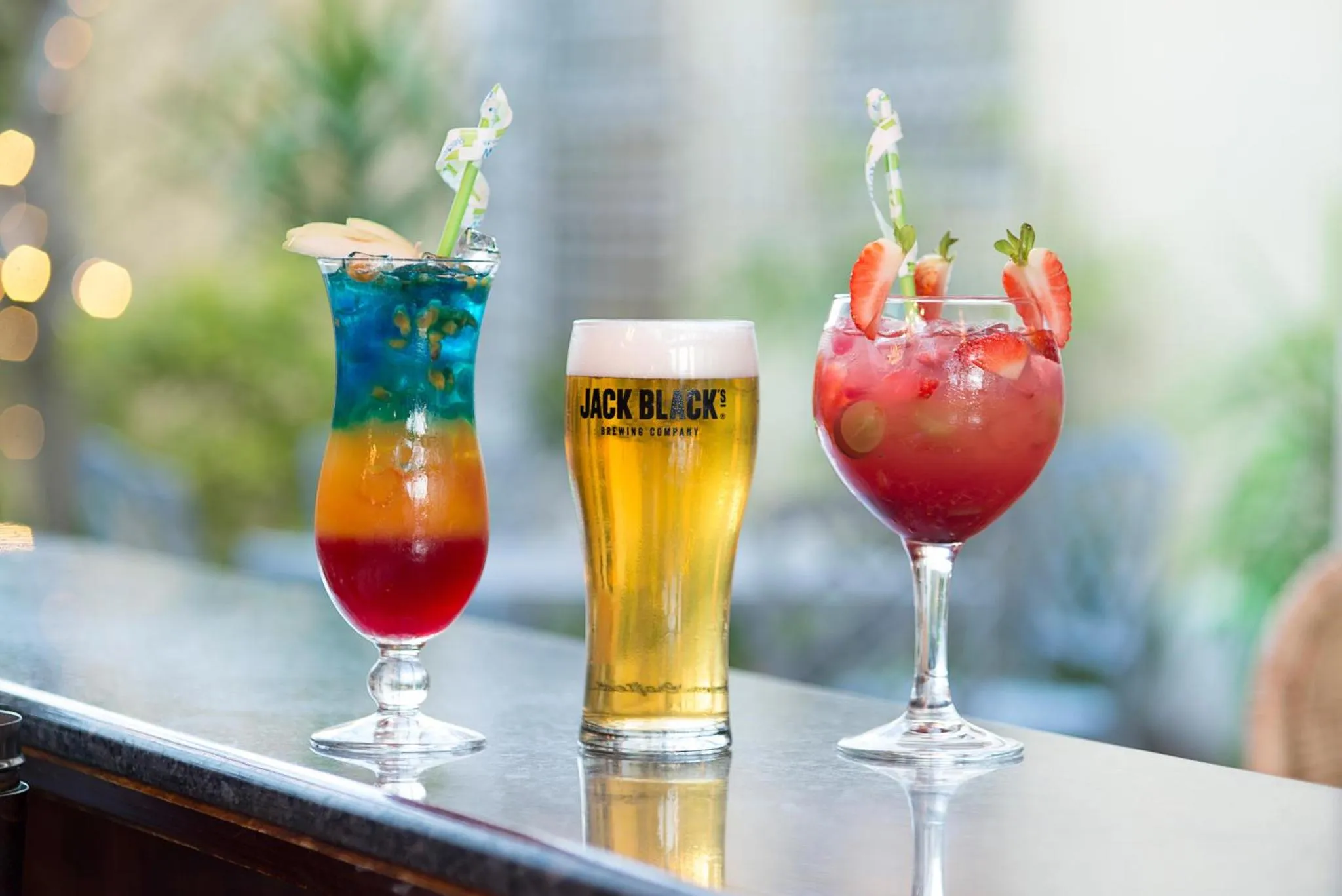 Trois verres colorés sont alignés sur un comptoir sombre.