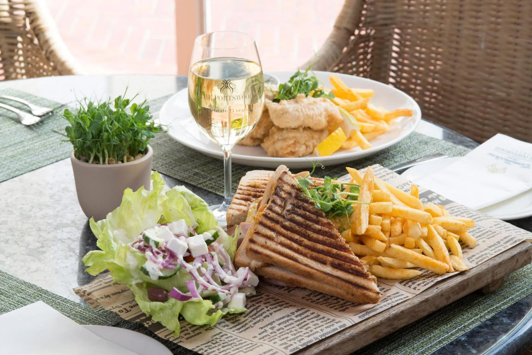 Une table est dressée avec un sandwich, une salade et des frites, accompagnés d'un verre de vin.