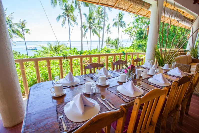 Une longue table est dressée pour un repas avec vue sur la mer et la végétation tropicale.