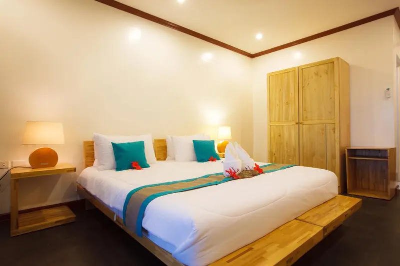 Une chambre lumineuse avec un grand lit recouvert de textiles clairs et turquoise.