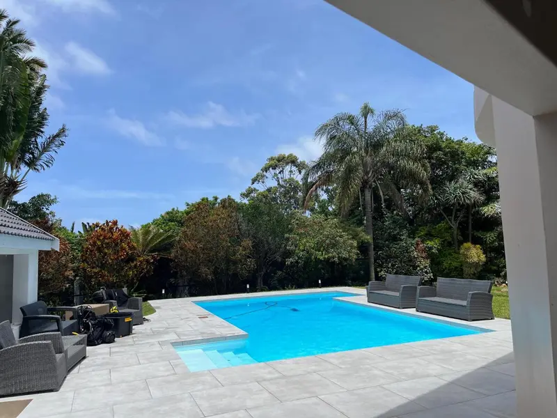Une piscine rectangulaire turquoise bordée d'une terrasse ensoleillée.