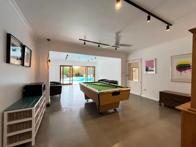 Espace de détente intérieur avec table de billard et vue sur une piscine.