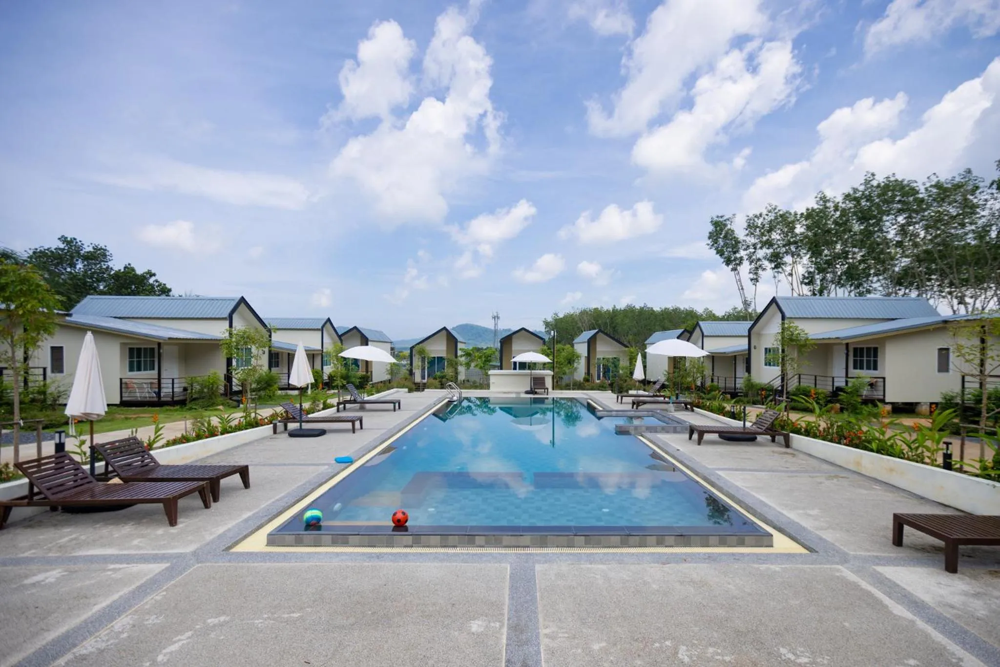 Vue d'une piscine bordée de transats devant des bungalows.