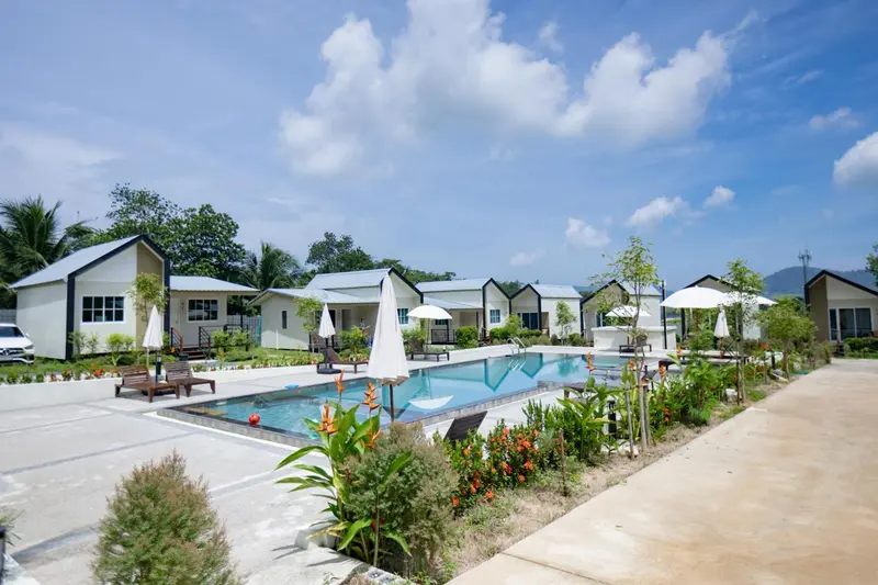 Petites maisons blanches avec toits sombres bordent une piscine rectangulaire.