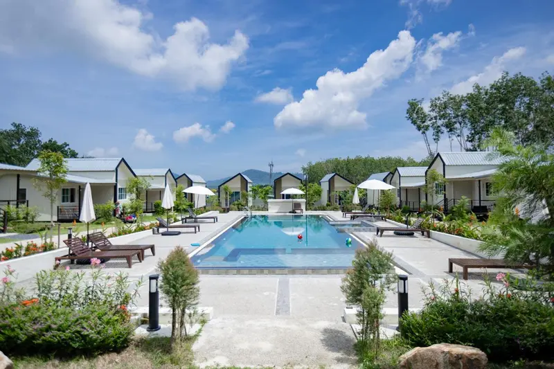 Une piscine rectangulaire bordée de transats et de bâtiments bas.
