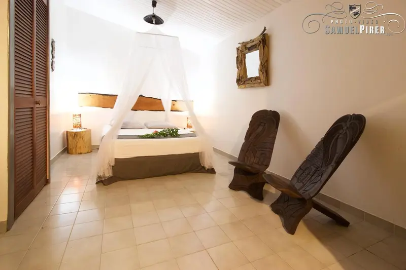Une chambre lumineuse avec un lit à baldaquin et des fauteuils sculptés.