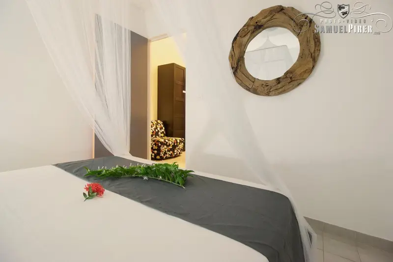 Une chambre lumineuse avec un lit recouvert de moustiquaire et un miroir rond en bois.