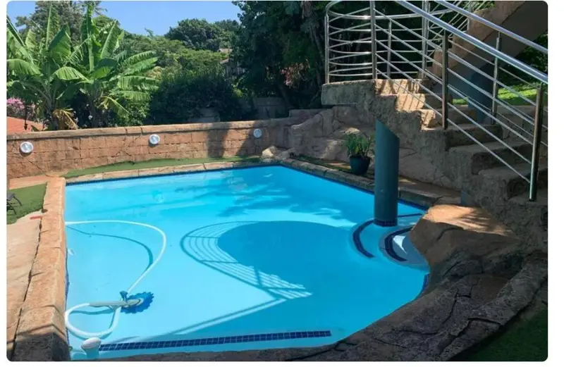 Une piscine rectangulaire entourée d'un muret en pierre et d'une végétation luxuriante.