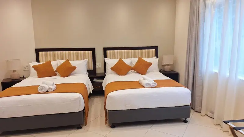 Deux lits jumeaux avec une décoration orange dans une chambre lumineuse.