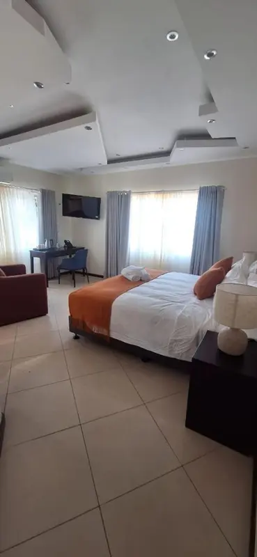 Une chambre lumineuse avec un lit recouvert d'une couverture orange et de coussins.