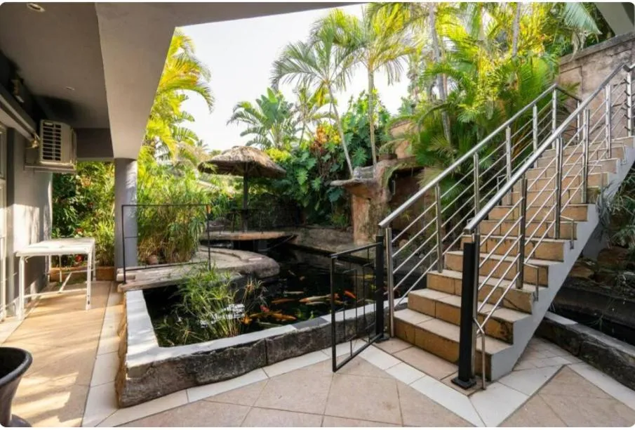 Un escalier mène à une terrasse ombragée avec un bassin de carpes koï.
