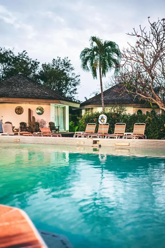 Transats oranges alignés au bord d'une piscine turquoise, végétation luxuriante en arrière-plan.