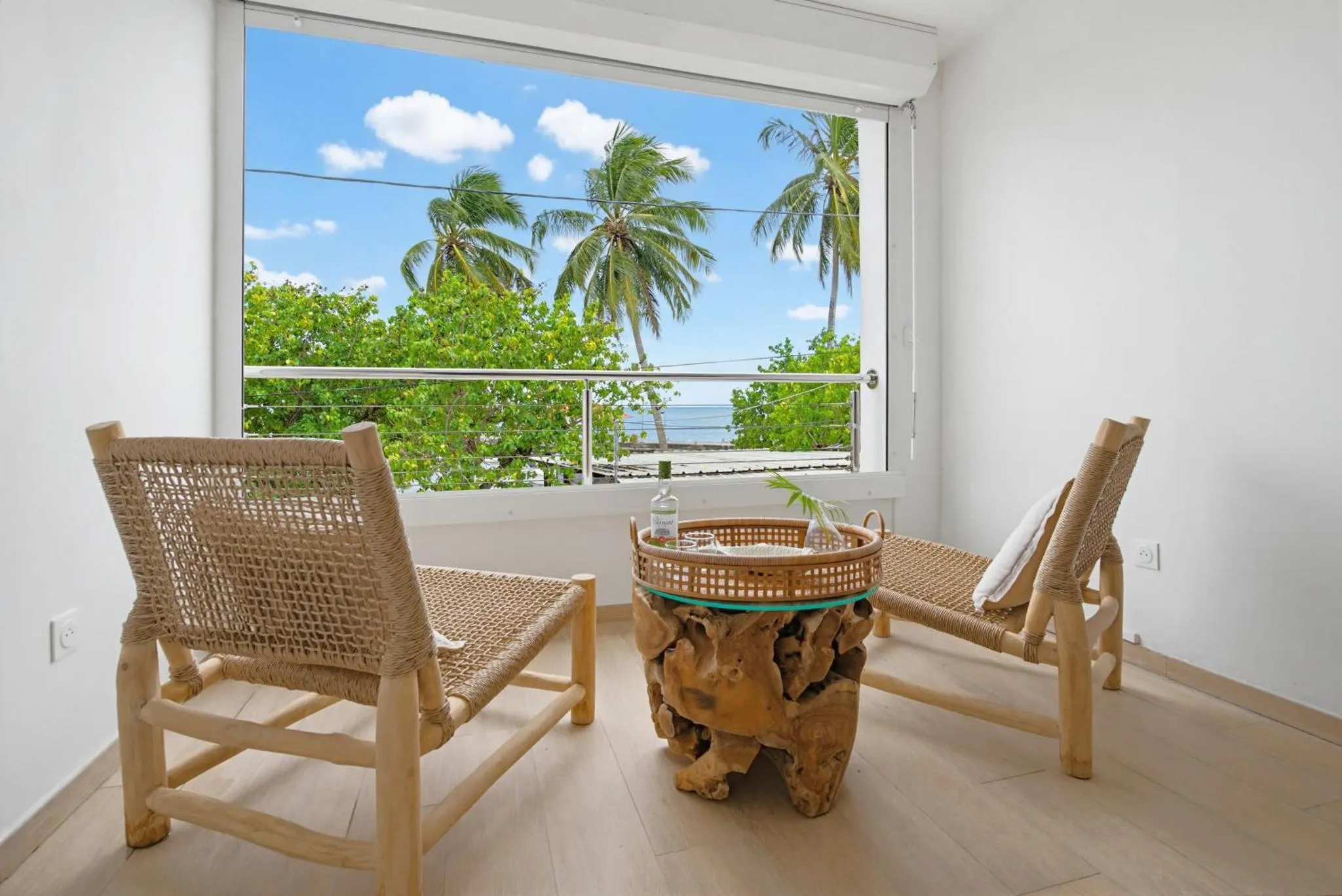Deux fauteuils en rotin face à une vue sur la mer et la végétation tropicale.