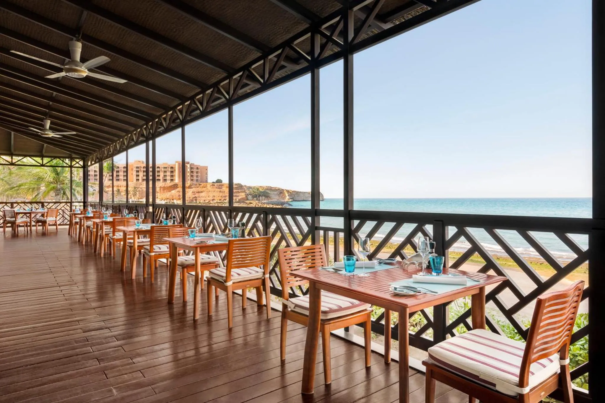 Terrasse ombragée avec tables et chaises donnant sur la mer.