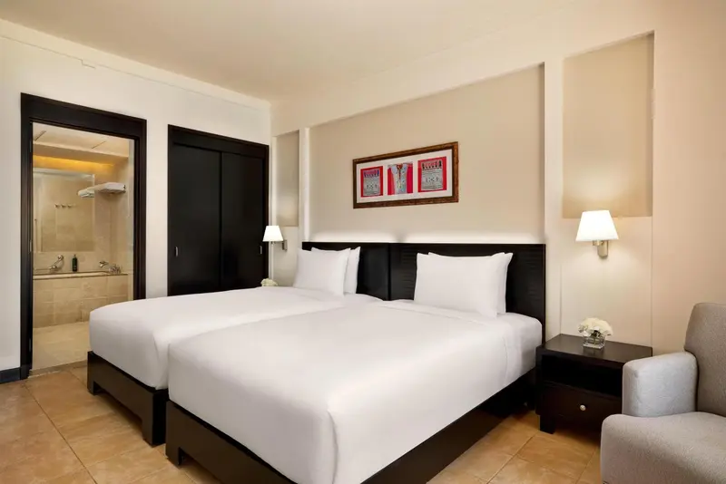 Chambre lumineuse avec deux lits simples et une salle de bain attenante.