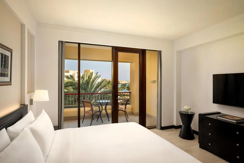 Chambre lumineuse avec un lit blanc et un balcon donnant sur une végétation luxuriante.