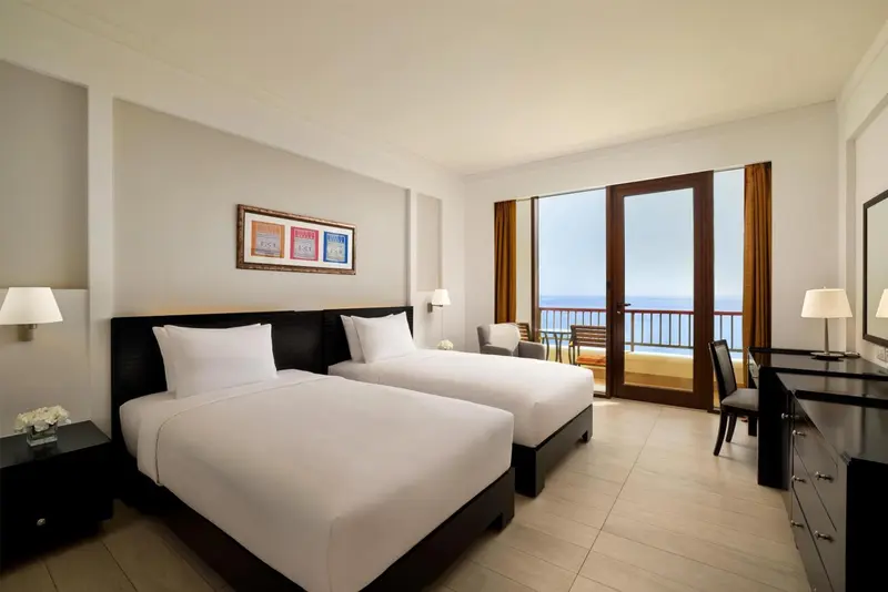 Chambre lumineuse avec deux lits simples et vue sur la mer.