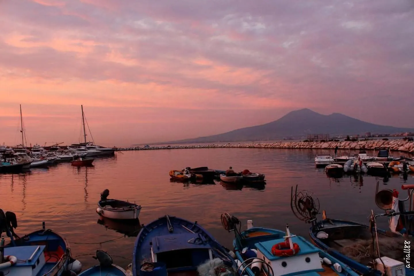 Un port de plaisance au coucher du soleil avec des bateaux amarrés et une île en arrière-plan.