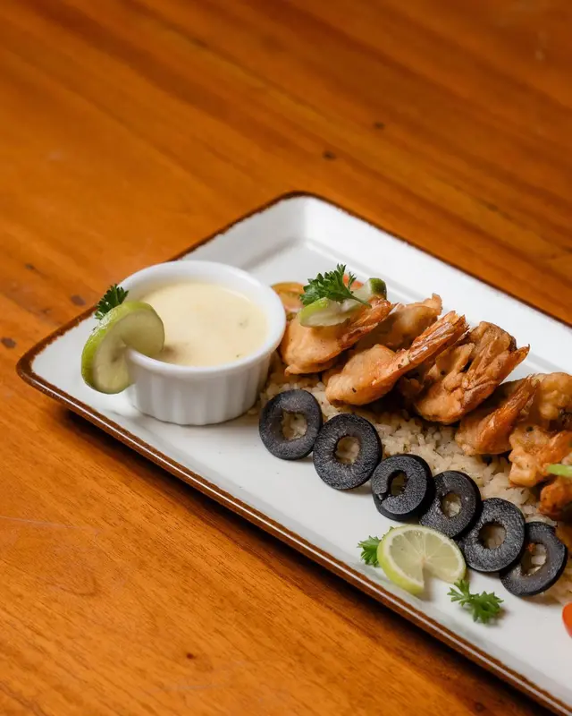 Assiette de crevettes grillées accompagnées d'une sauce et de légumes.