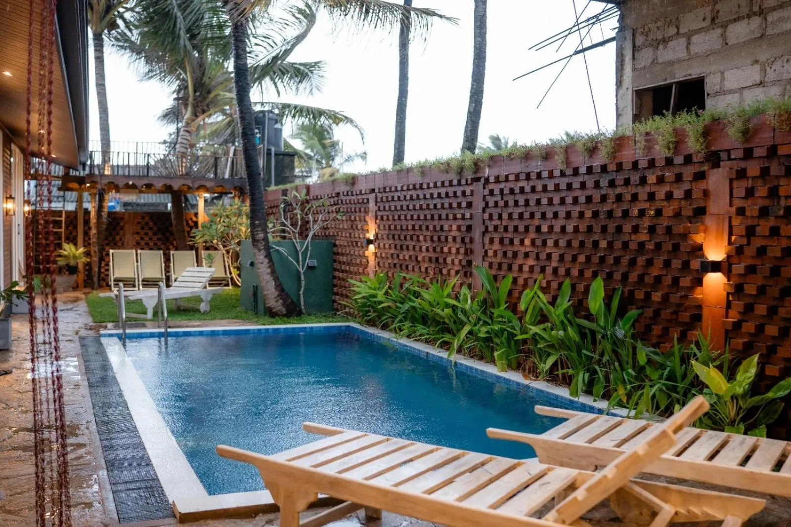 Petite piscine rectangulaire entourée de chaises longues en bois et de végétation tropicale.
