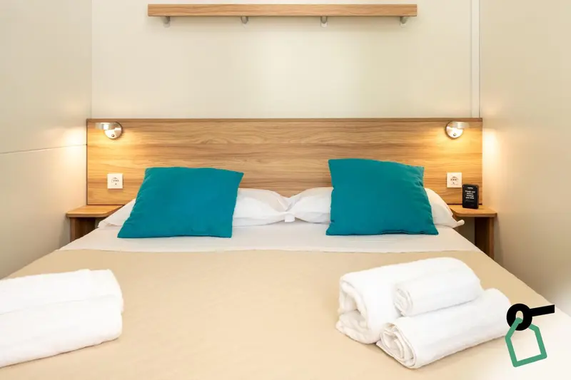 Un lit double avec des oreillers verts et des couvertures blanches dans une chambre lumineuse.
