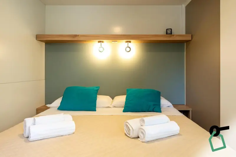 Un lit avec des oreillers turquoise et des serviettes blanches est prêt dans une chambre.