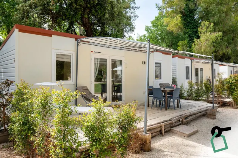 Mobil-homes alignés dans un parc verdoyant avec des terrasses équipées de mobilier de jardin.