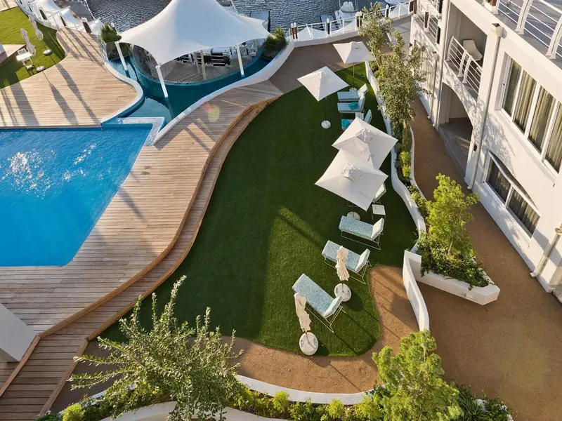 Vue aérienne d'une piscine et d'une pelouse verdoyante avec des transats blancs.