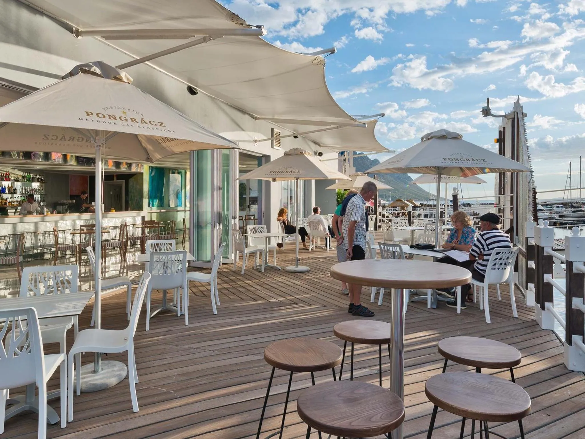 Terrasse ensoleillée avec tables et chaises près d'un bar en bord de mer.