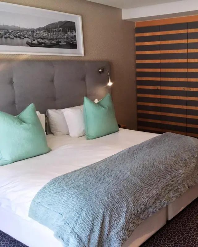 Une chambre avec un grand lit recouvert d'une couverture claire et de coussins verts.