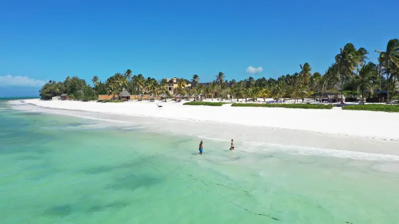 Plage de sable blanc bordée d'une eau turquoise et de végétation tropicale.