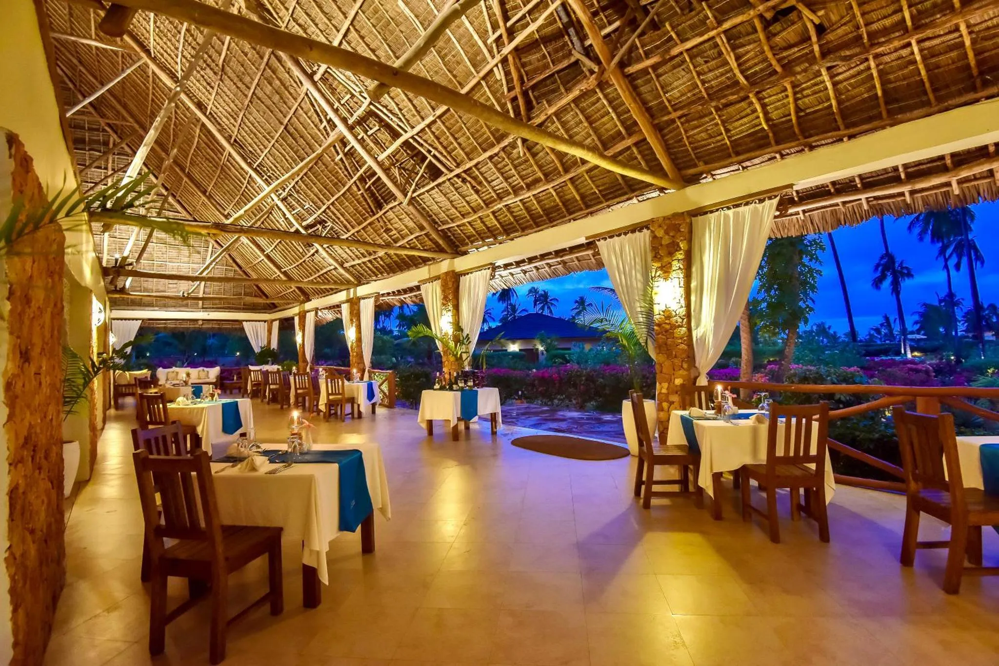 Une salle de restaurant à ciel ouvert avec des tables dressées et une vue sur la mer au loin.